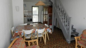 Uma área de refeições com mesa e cadeiras, uma cozinha ao fundo e uma escada.