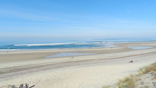 Uma extensa praia de areia com ondas suaves e céu azul límpido.