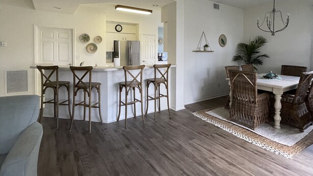 A spacious living room with a large dining table and chairs, a kitchen area with bar stools, and a chandelier. - Beautifully updated, gated community, minutes from the gulf beaches (Bonita Springs)