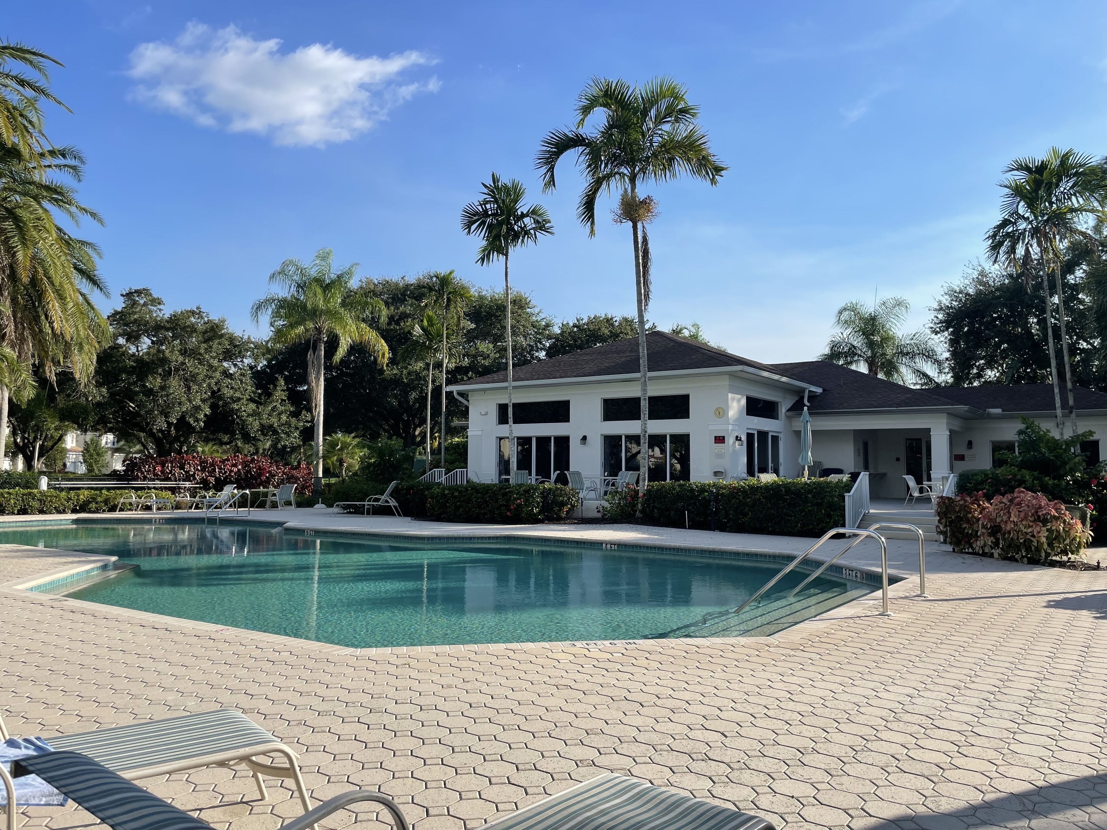 A swimming pool with hexagonal tiles, lounge chairs, and a building with a white exterior and dark roof.