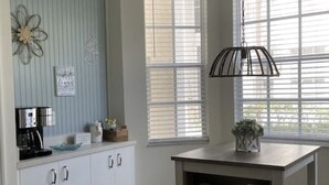A kitchen with white cabinets, a coffee maker, and a small table with shelves. - Beautifully updated, gated community, minutes from the gulf beaches (Bonita Springs)