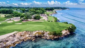 A coastal golf course with a clear view of the ocean, a well-maintained fairway, and a rocky shoreline.