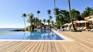 A pool area with a wooden deck, lounge chairs, and palm trees.