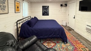 Een kamer met een bed, een leren zwarte bank, een tapijt met patroon en een televisie aan de muur.