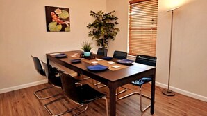 A dining area with a long table, chairs, a plant, and a painting on the wall. - Cozy Spacious Corporate Housing 4 BR|2.5 Bath|Loft|Office|Near Tesla (Austin)