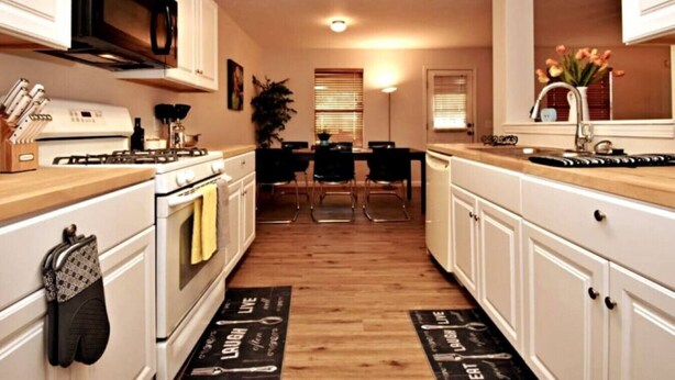 A compact kitchen with white cabinets, a microwave, and a stove. There is a dining area with a table and chairs. - Cozy Spacious Corporate Housing 4 BR|2.5 Bath|Loft|Office|Near Tesla (Austin)