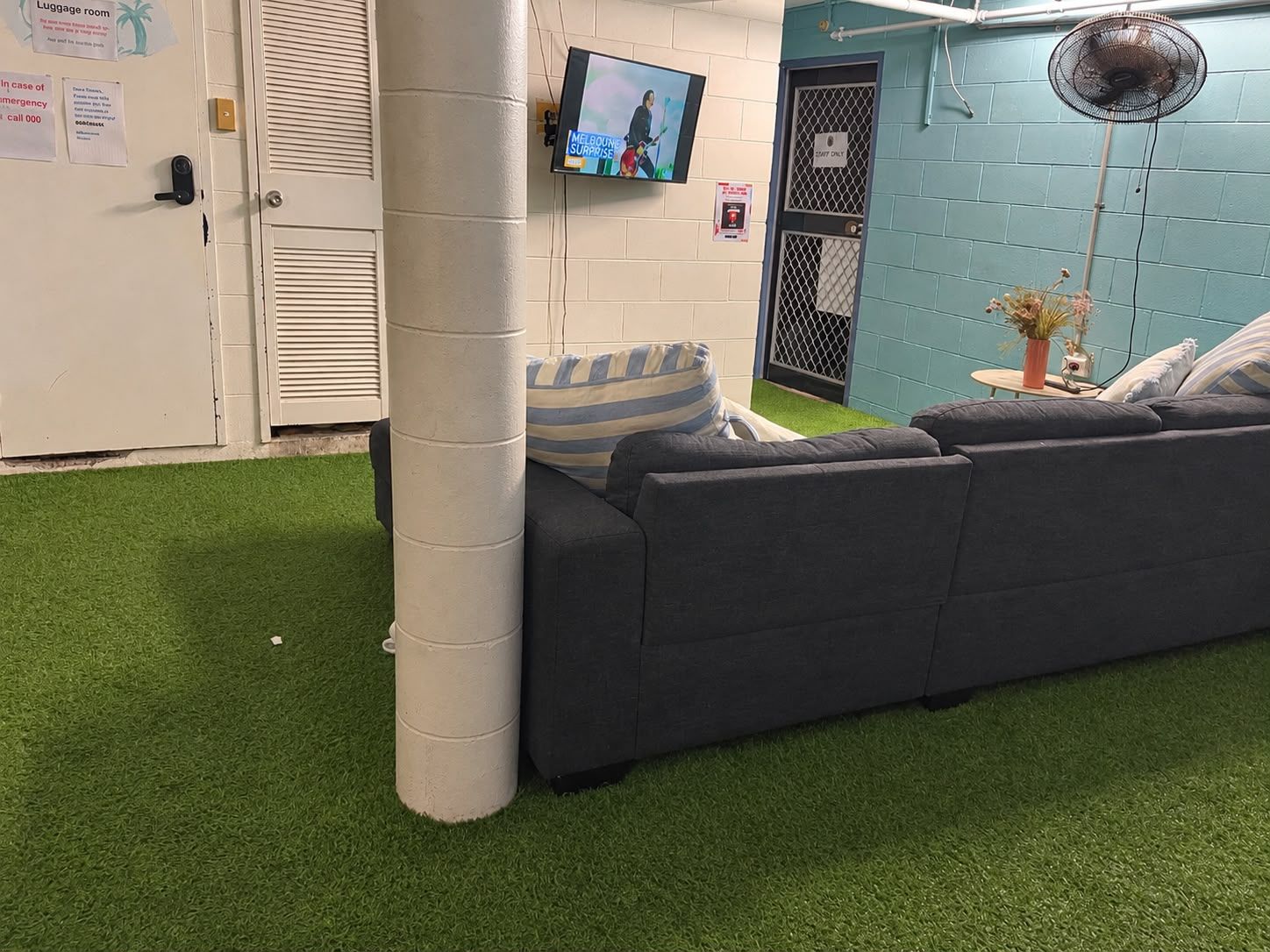 A room with a grey sofa, a white pillar, a television mounted on the wall, and a small table with a plant.