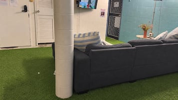 A room with a grey sofa, a white pillar, a television mounted on the wall, and a small table with a plant.