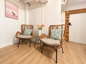A room with two wicker chairs, a small table with a vase of flowers, and a painting on the wall. - The Espy Hostel (Cairns)