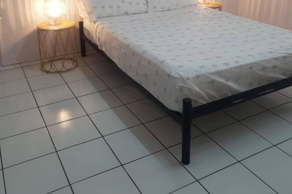 Un dormitorio con cama, dos lámparas de noche, un cuadro colgado en la pared de una playa y suelo de baldosas.