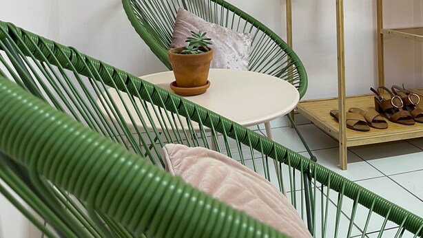 A room with a green chair, a small table with a potted plant, and a wooden shelf with hanging towels. - The Espy Hostel (Cairns)