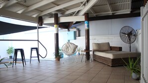 A spacious patio with a cushioned seating area, a fan, and potted plants. - The Espy Hostel (Cairns)