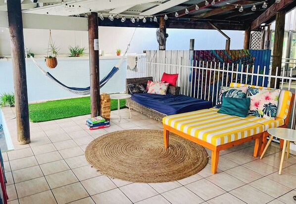 Un espacio al aire libre techado con una hamaca, un banco acolchado y una pequeña mesa.