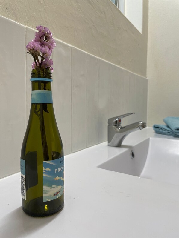A bottle of wine with a label featuring a mountain and sky design, placed on a bathroom counter next to a sink. - The Espy Hostel (Cairns)