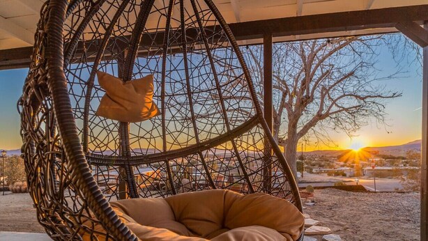 A hanging chair with a cushion, overlooking a sunset view through large windows. - ✧VIEWS✧ 6min to Joshua Tree walk to bars + firepit  (Twentynine Palms)