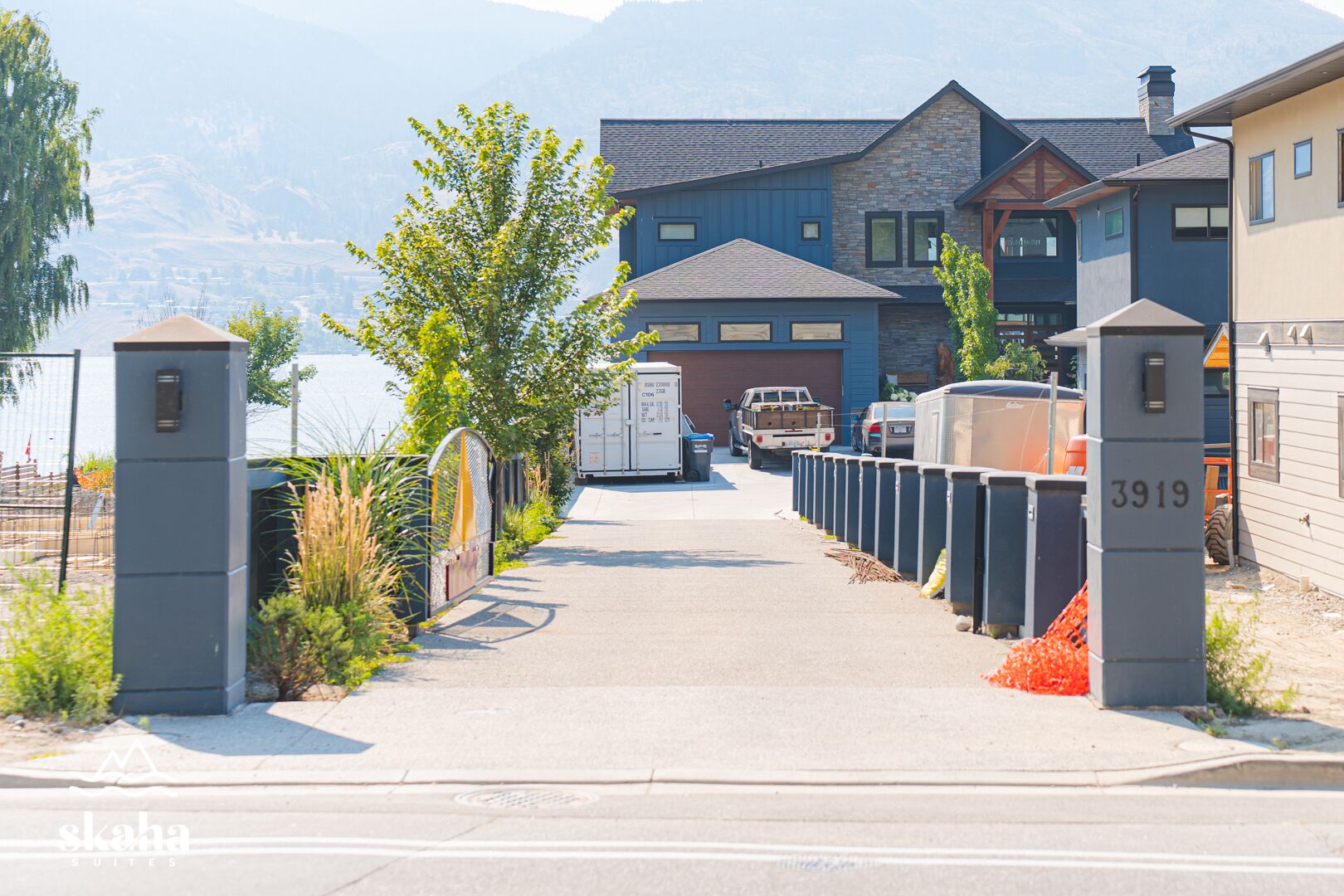 Une allée fermée par un portail mène à un bâtiment moderne doté d’une façade en pierre et offrant une vue sur la montagne.