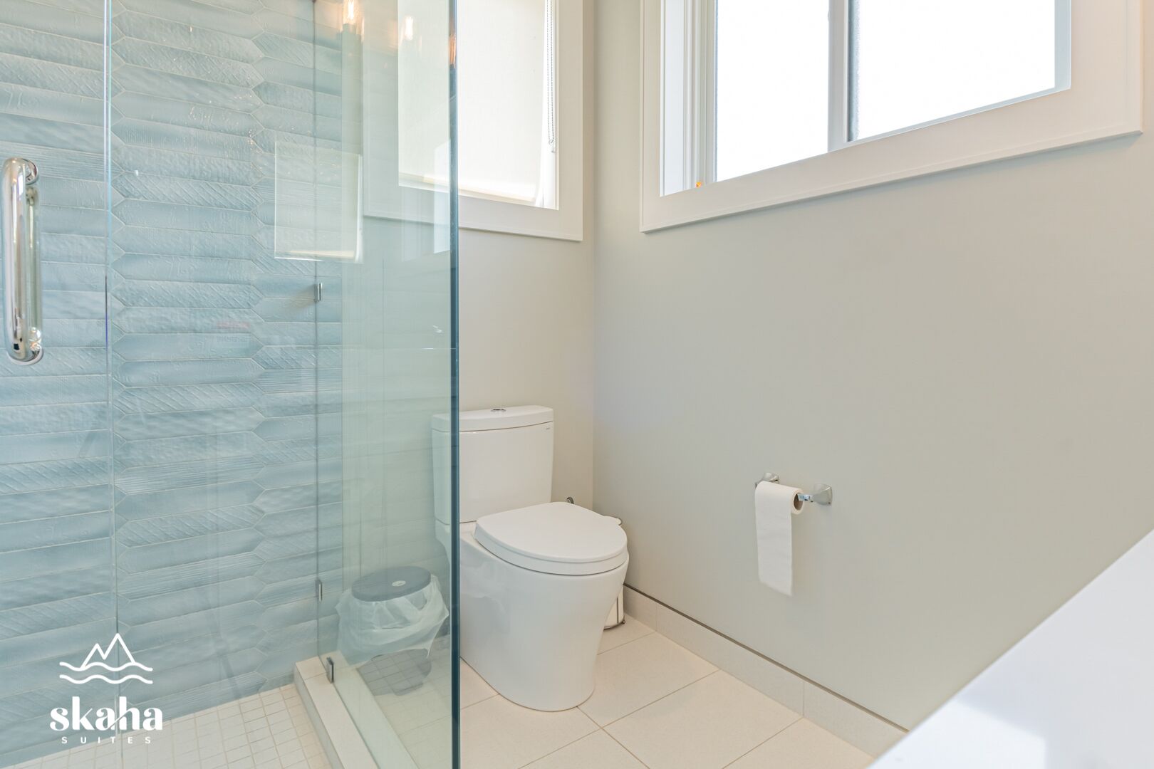 A modern bathroom with a glass shower enclosure, a toilet, and a window providing natural light.