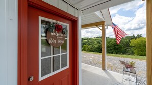 A red door with a welcome sign, an American flag, and a view of a green landscape. - 331 Acres of Comfort & Rest, ❤ of the Bluegrass- 12 mins from ARK w/Hot Tub  (Corinth)
