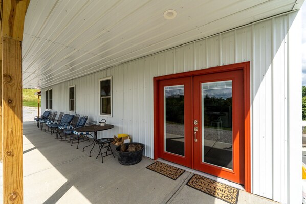A covered outdoor seating area with a red door, a table, and several chairs.