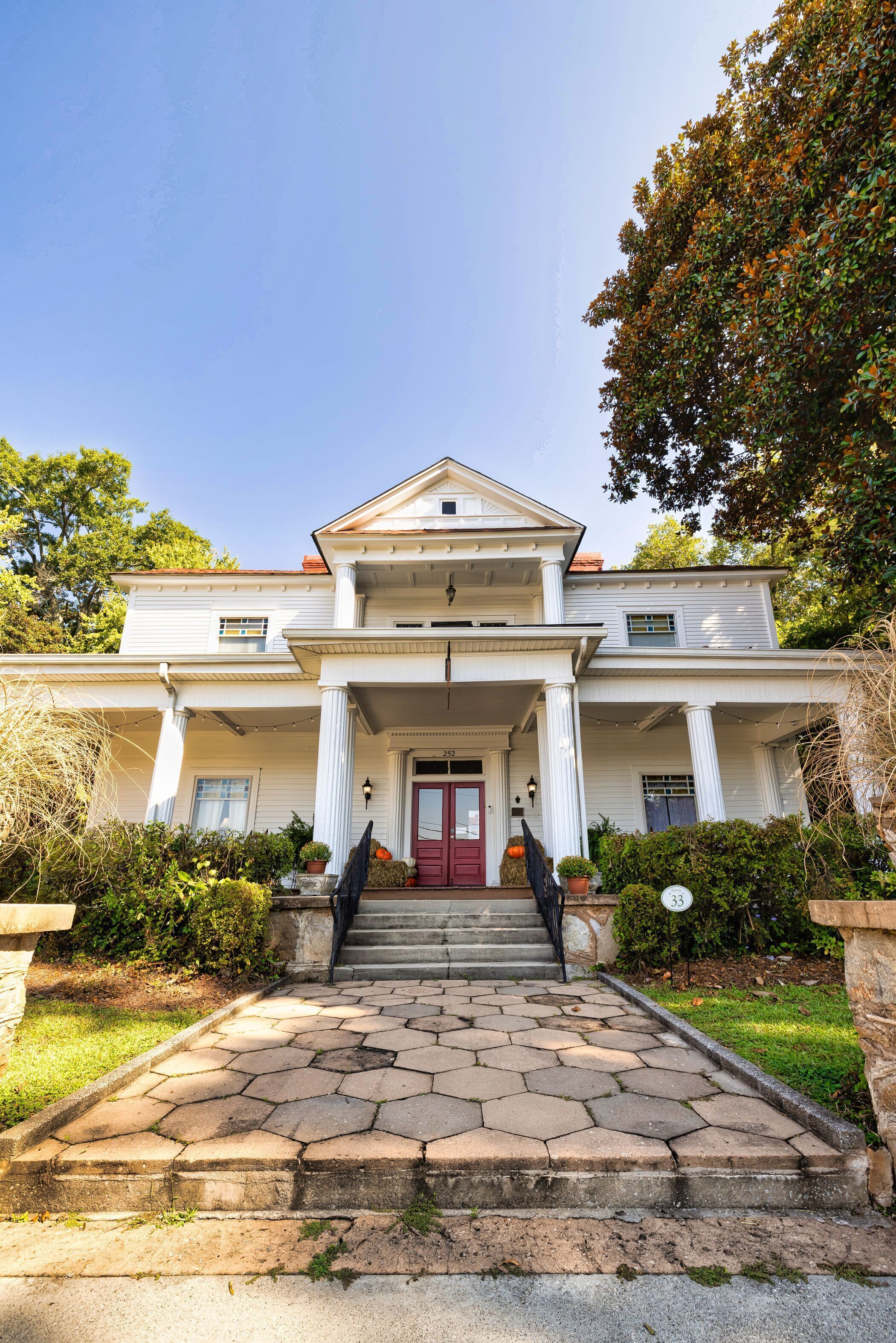 A two-story house with a red door, white columns, and a stone staircase leading to the front door.