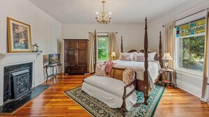 A spacious bedroom with a four-poster bed, a fireplace, and a large window with curtains.
