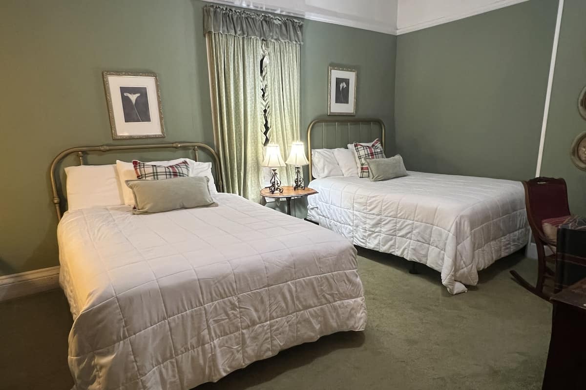 Two single beds with white bedding, a nightstand with a lamp, and a chair in a room with green walls.