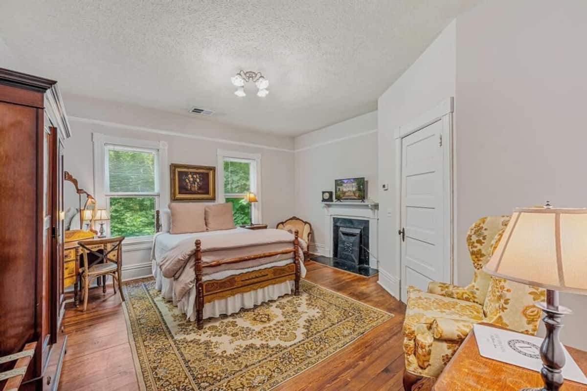 A bedroom with a wooden bed, a fireplace, a large window, and a chandelier.