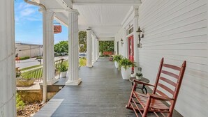A covered porch with white columns, a bench, and potted plants. - The Veranda Historic Inn (Senoia)