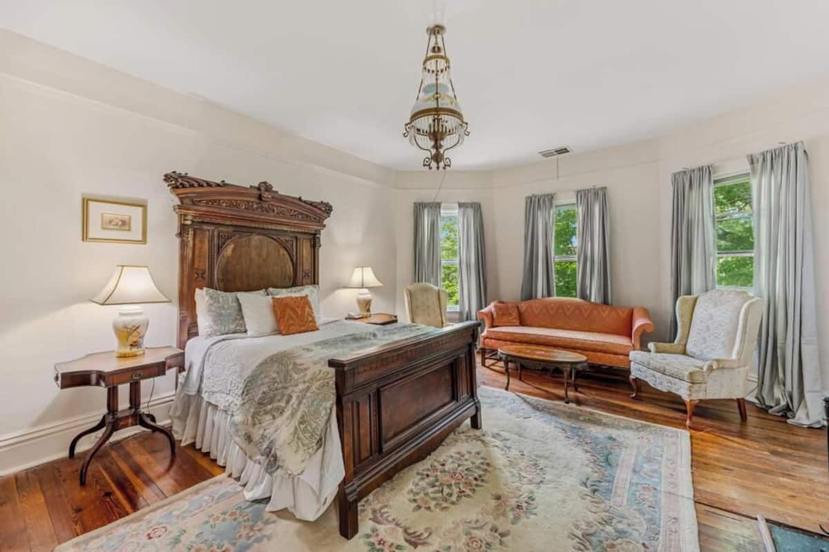 A bedroom with a large wooden bed, a sofa, a chair, and a chandelier.