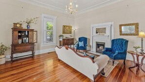 A spacious living room with hardwood flooring, a white sofa, a blue armchair, a fireplace, and a chandelier. - The Veranda Historic Inn (Senoia)