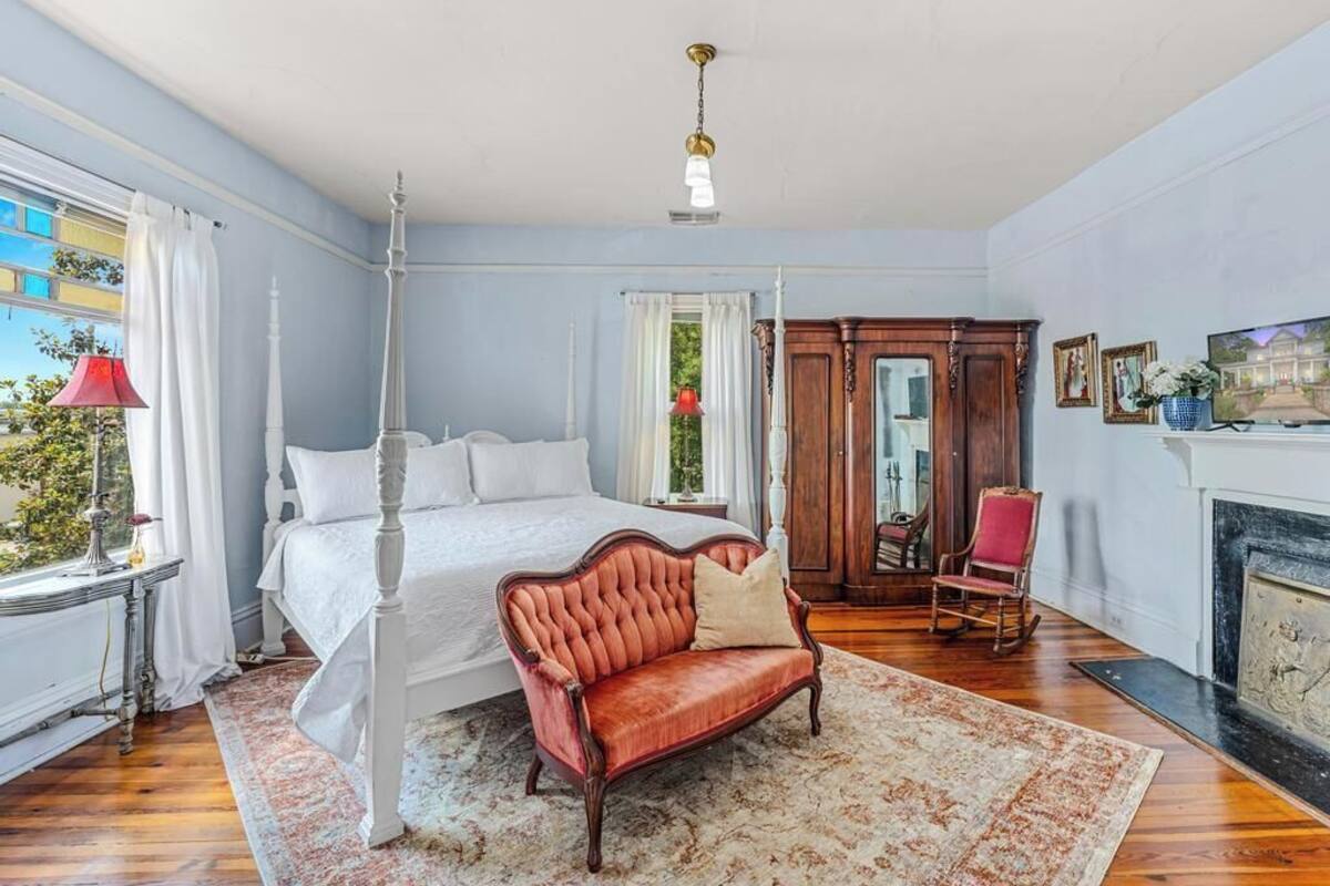 A bedroom with a four-poster bed, a red leather sofa, a fireplace, and a view of the outdoors.