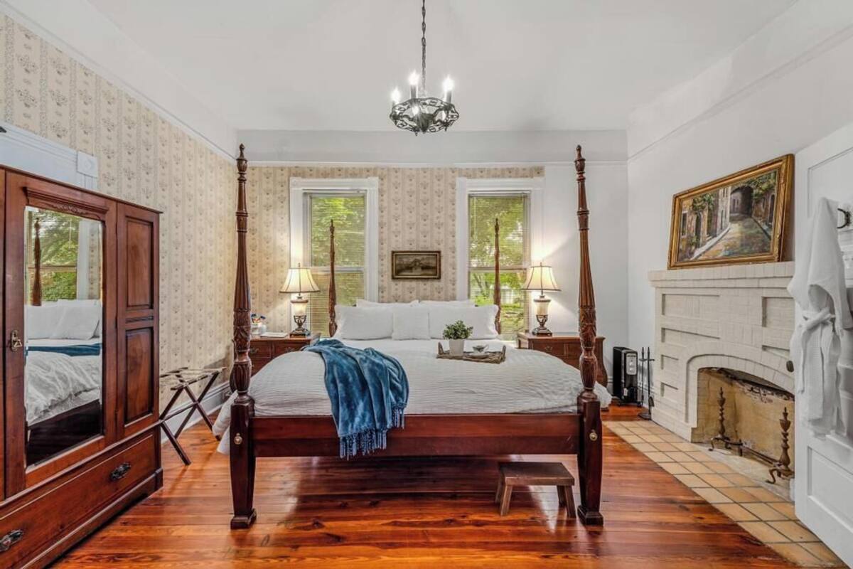 A four-poster bed with a wooden frame, two bedside tables with lamps, a fireplace, and a large mirror.
