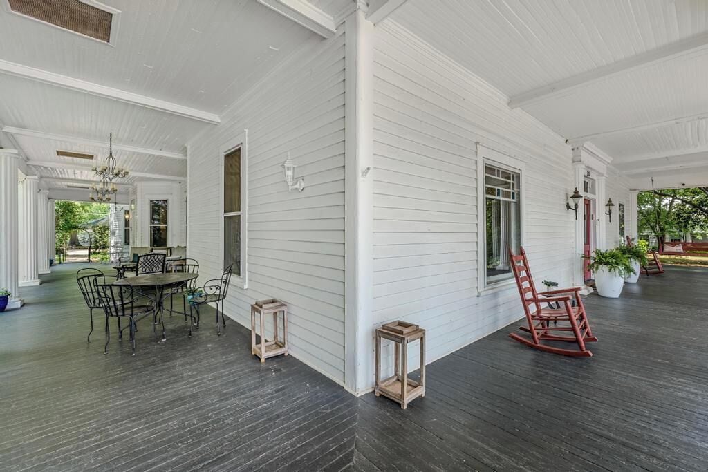 A spacious porch with a dining table and chairs, a rocking chair, and potted plants.