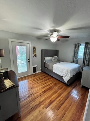 Une chambre à coucher avec un lit, un ventilateur de plafond, une fenêtre avec des rideaux et une porte avec des stores.