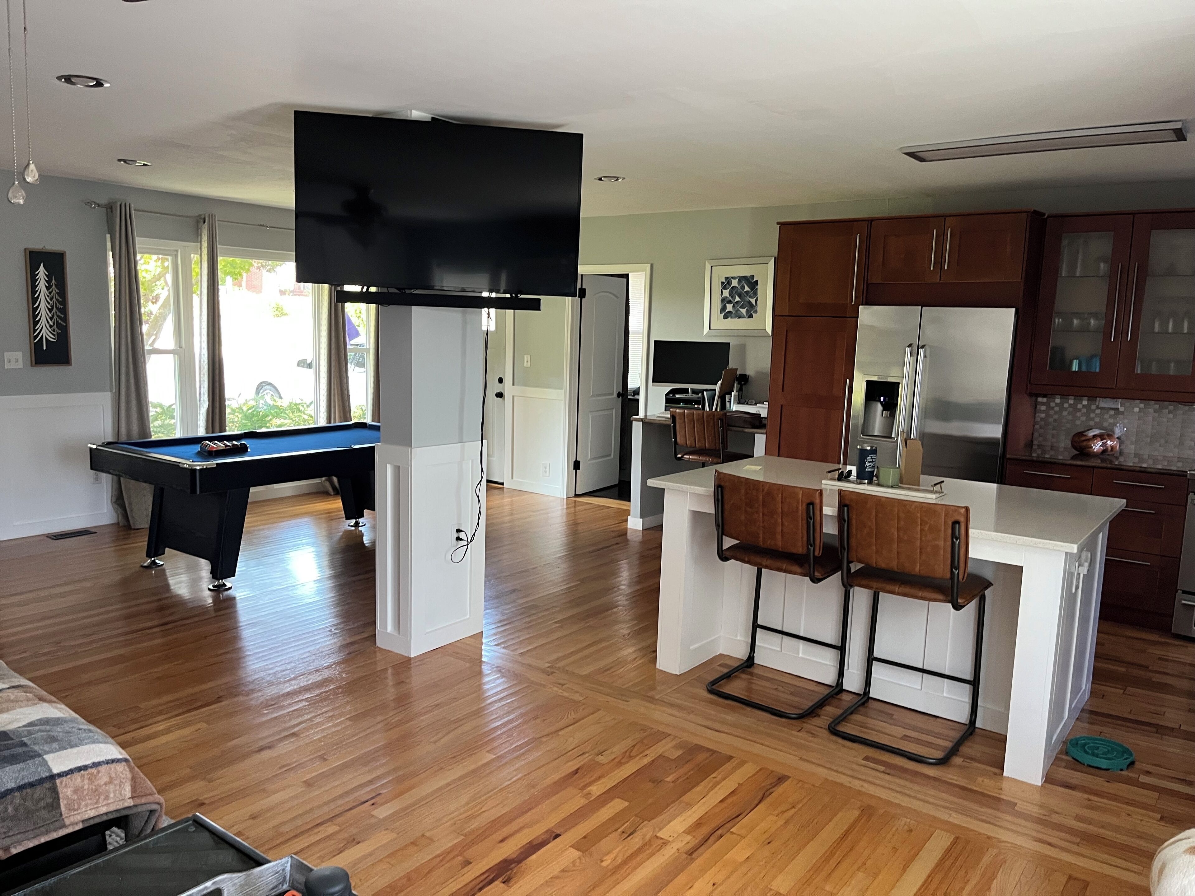 A modern kitchen with a central island, wooden flooring, and a pool table in the living area.