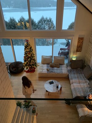 A spacious living room with a large window overlooking a snowy landscape, a Christmas tree, and a cozy seating area.