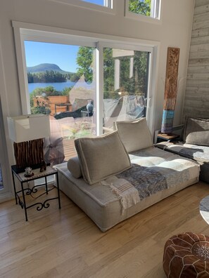 A cozy living room with a large window offering a scenic view of a lake and mountains.