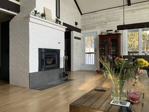 A modern living room with a fireplace, wooden flooring, and a dining area with a table and chairs.