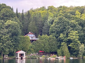 A lakeside cabin with a deck, surrounded by dense forest.