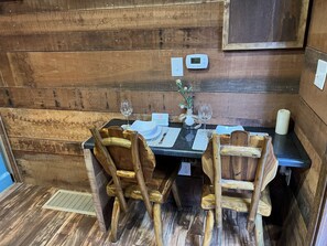A wooden cabin interior with a dining table set for two, wooden chairs, a vase with flowers, and a digital thermostat on the wall. - RR Vacation on the Rocks (Blue Ridge)
