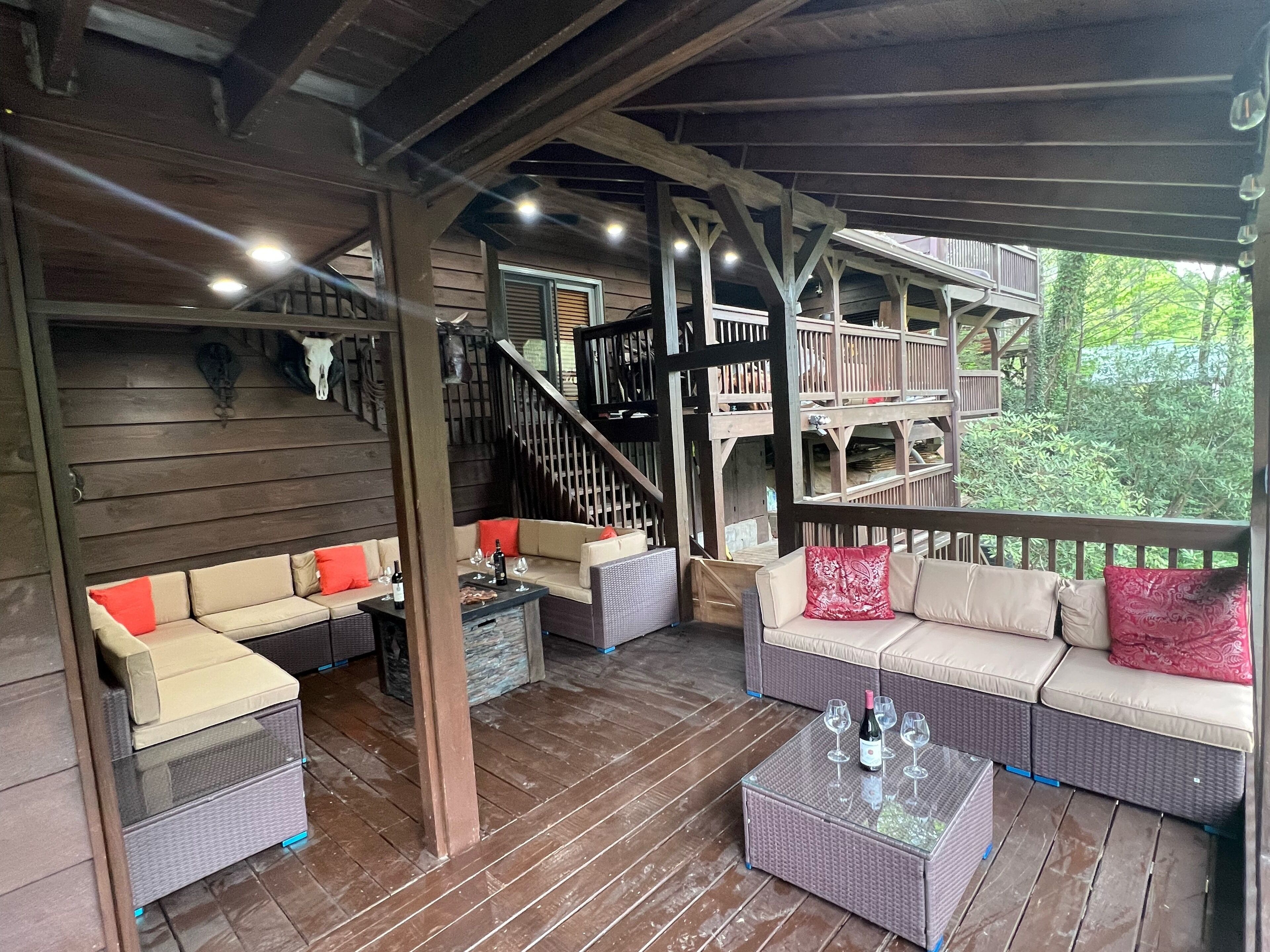 A covered outdoor seating area with wicker furniture, a wooden staircase, and a view of greenery.