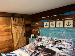A bedroom with a wooden wall, a blue dresser, and a bed with a wolf-themed bedspread. - RR Vacation on the Rocks (Blue Ridge)