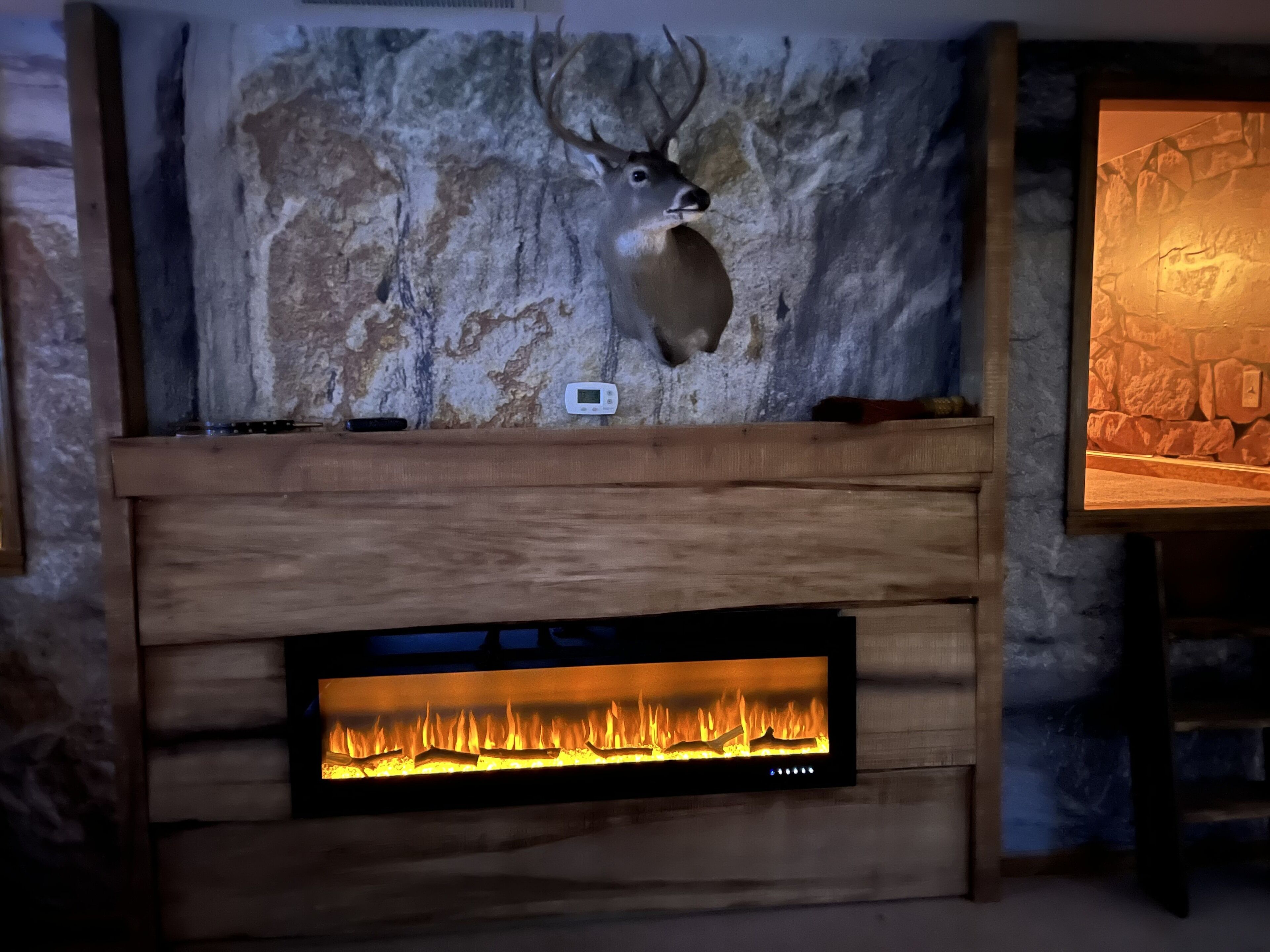 Een haard met daarboven een decoratie van een hertenhoofd, een thermostaat en een achtergrond van een stenen muur.