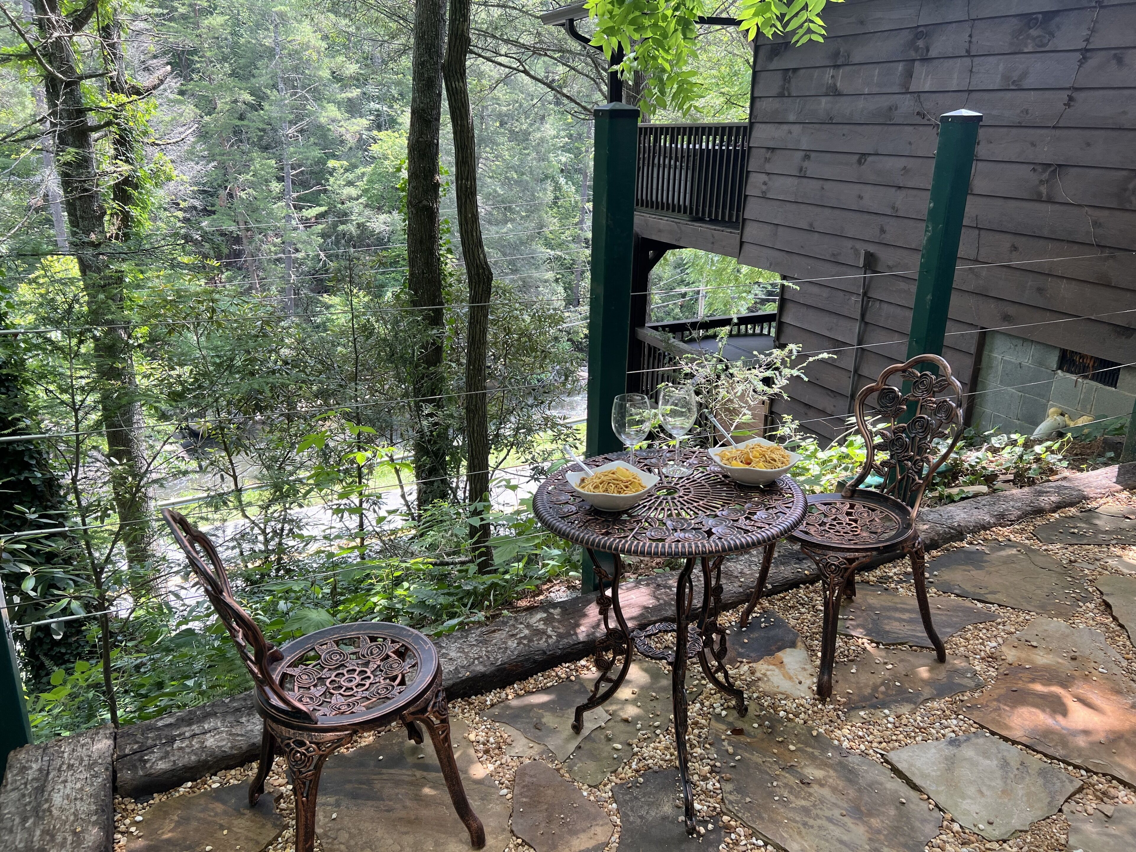 An outdoor patio with a table and chairs, surrounded by a wooden fence and lush greenery.