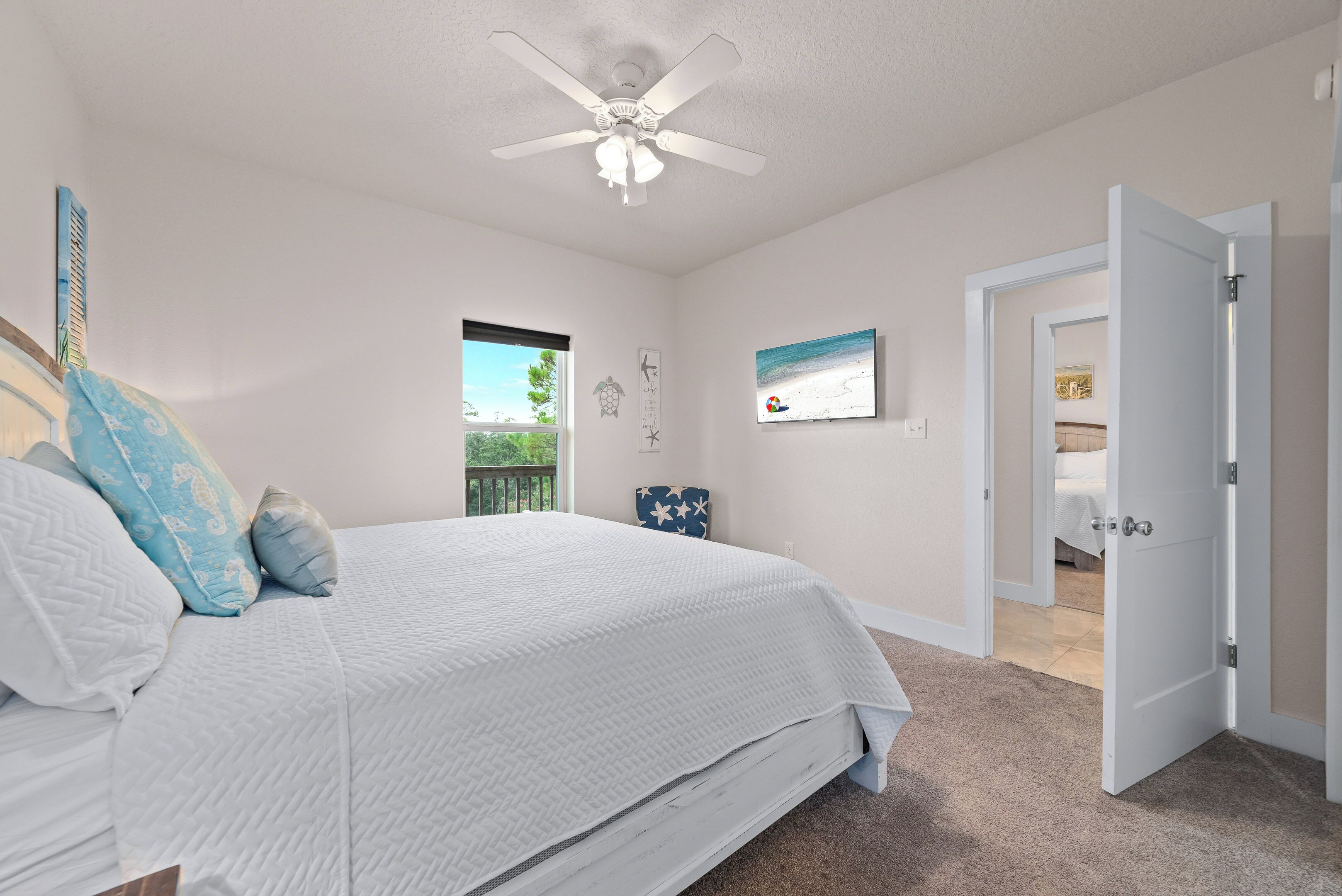 A bedroom with a bed, a ceiling fan, a window, a door, and a wall-mounted picture.