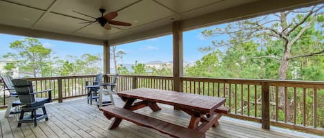 A wooden deck with a picnic table and chairs, a ceiling fan, and a view of trees and hills.