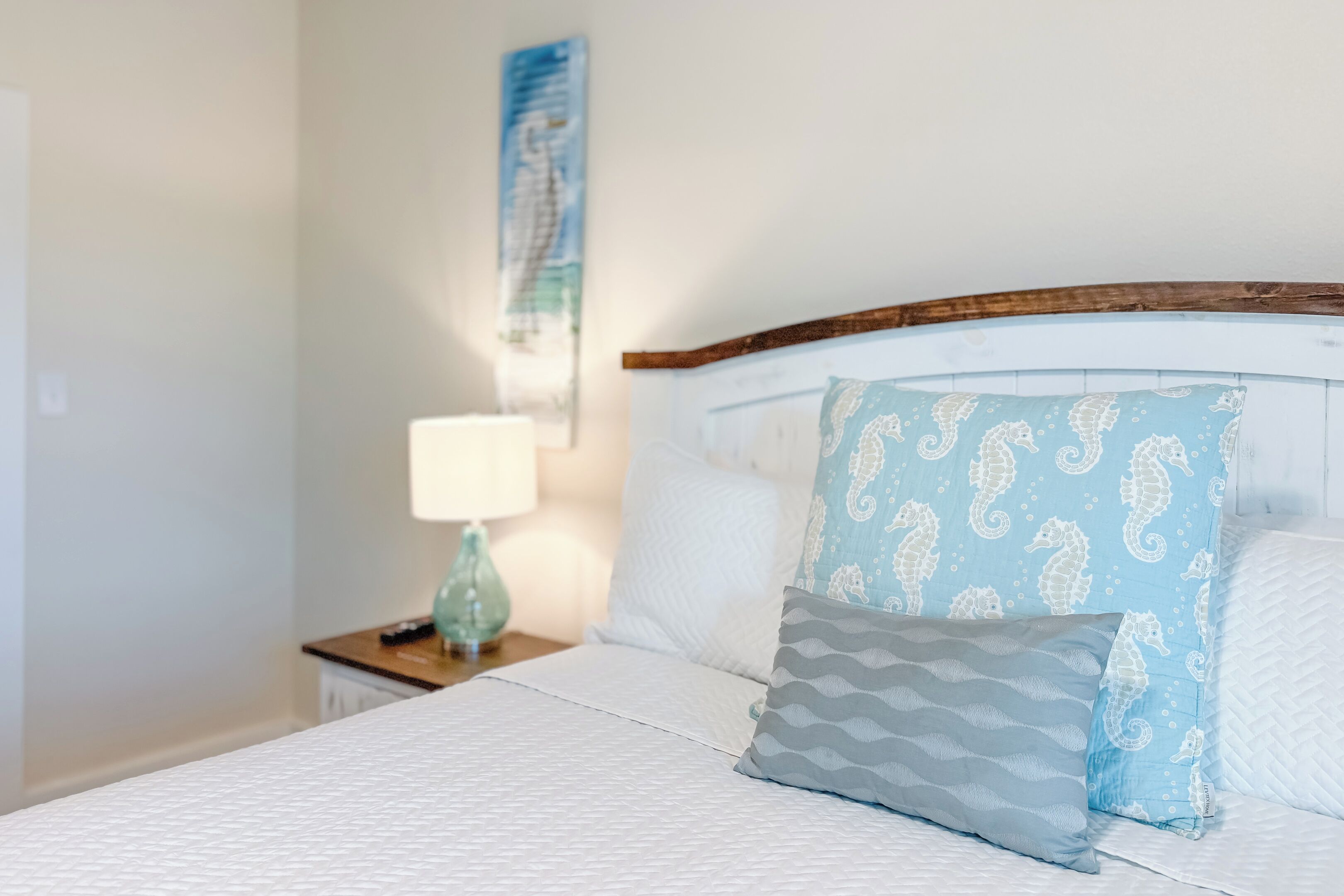 A neatly made bed with a white and gray patterned bedspread, a wooden headboard, and decorative pillows with a seahorse pattern.