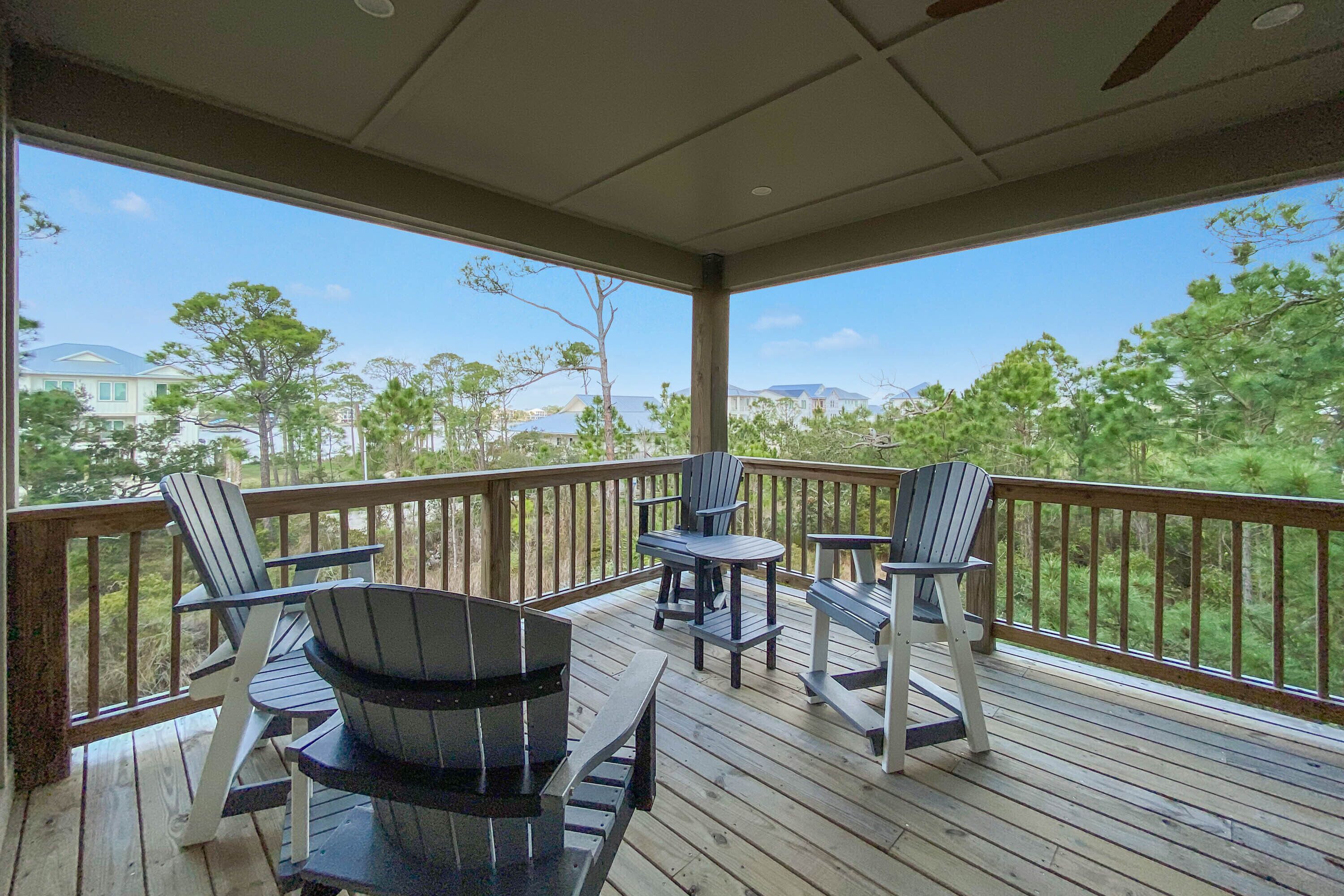 A covered deck with Adirondack chairs and a table, overlooking a residential area with trees and houses.