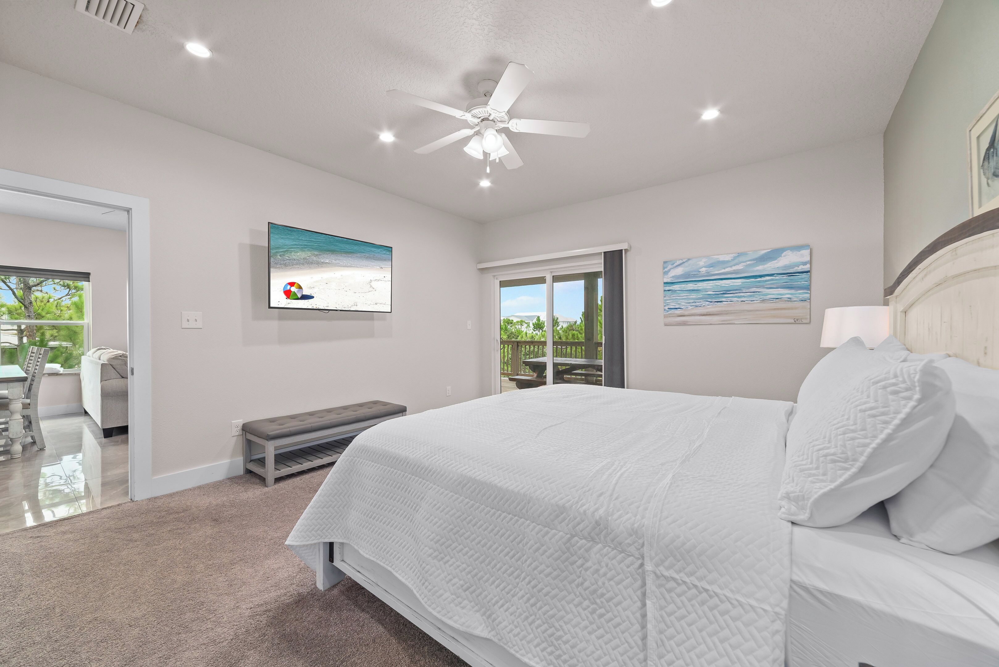 A bedroom with a large bed, a ceiling fan, and two paintings on the walls.