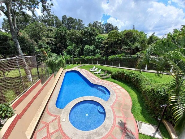 Relax by the serene pool surrounded by lush greenery and a well-manicured lawn.